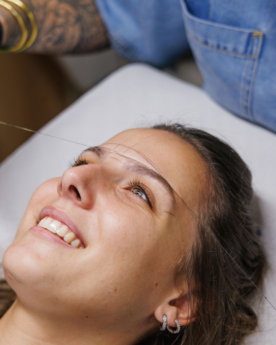 Cliente souriante pendant une épilation au fil des sourcils