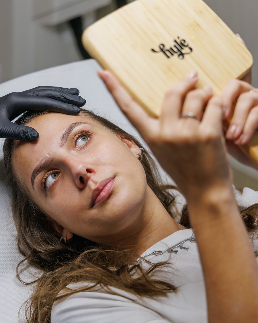 Cliente découvrant le résultat de son maquillage permanent des sourcils au miroir Hylé